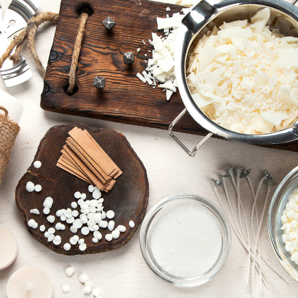 Flat lay av material för ljustillverkning med sojavaxflingor, bomullsvekar, kanelstänger, kryddnejlikor och trädetaljer i en rustik, naturlig stil för handgjorda doftljus.