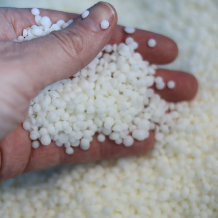 Hand som håller sojavax-pellets vid tillverkning av handgjorda doftljus i Sverige