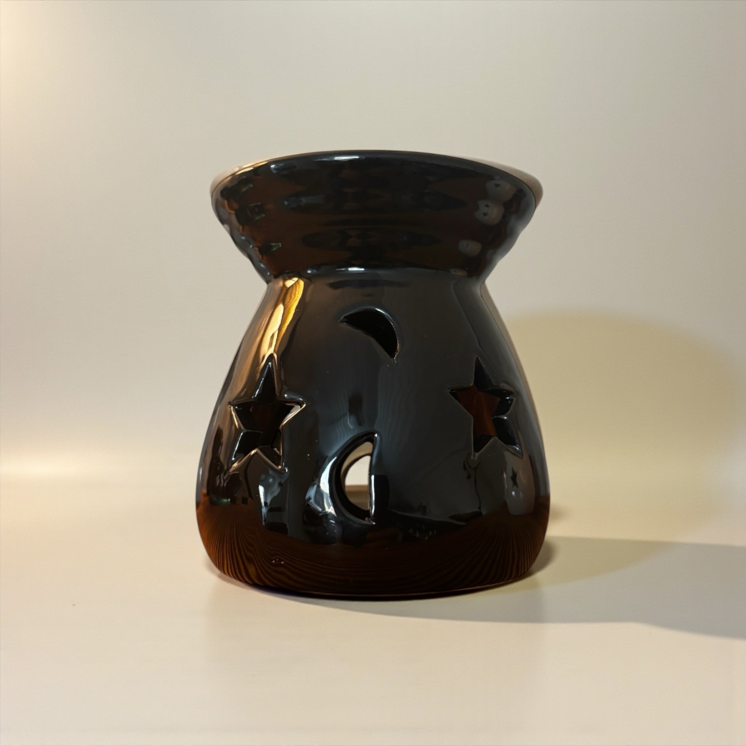 En svart aromalampa som har små hål i forma av månar och sjärnor. Lampan står på en ljus duk.