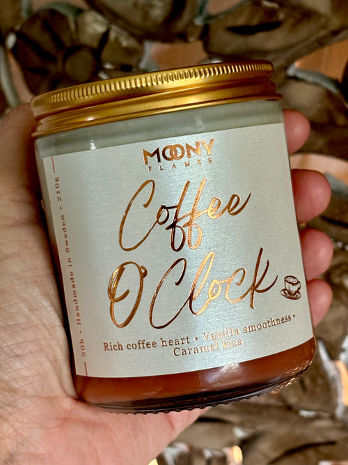 Doftljus Coffee O´Clock i genomskinlig glasburk med guldlock som hålls i handen - Moony Flames.