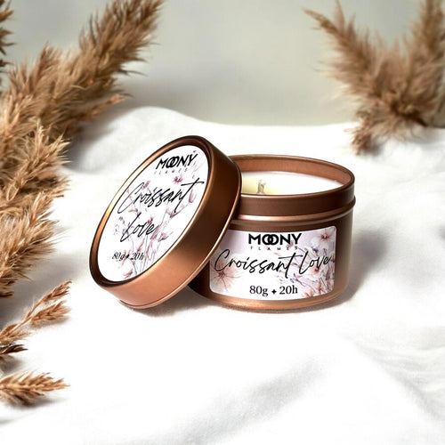 Doftljus Croissant Love metallburk som står på en vit duk med torkade blommor i bakrunden. Reseljus - Moony Flames