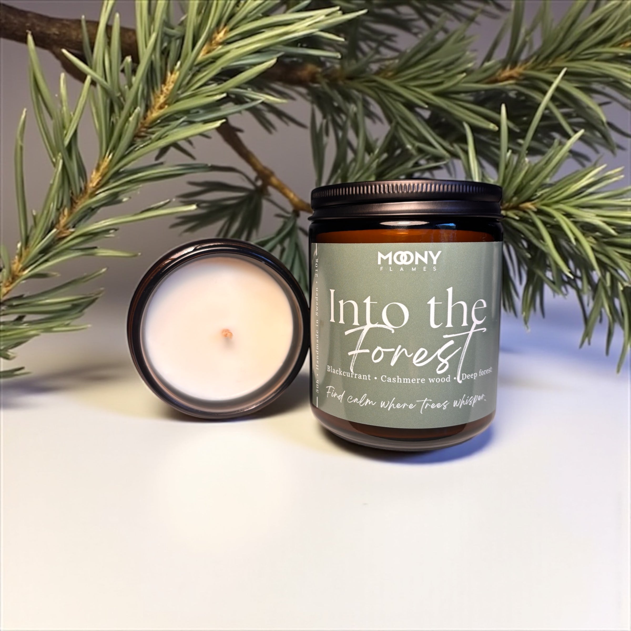 Doftljus Into the Forest från Moony Flames. Stor på en vit yta med skogsdekoration i bakgrunden.