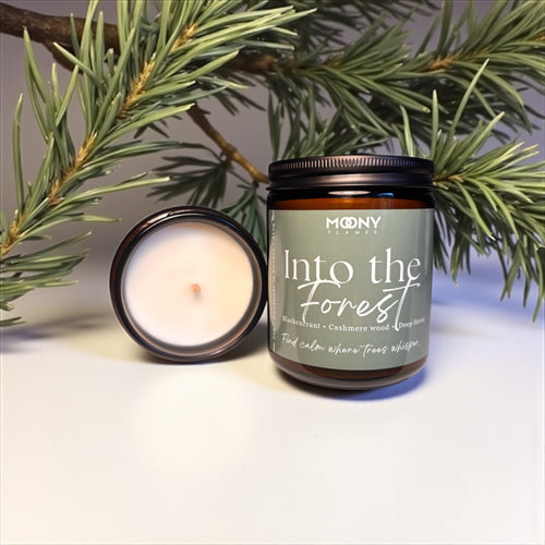 Doftljus Into the Forest från Moony Flames. Stor på en vit yta med skogsdekoration i bakgrunden.