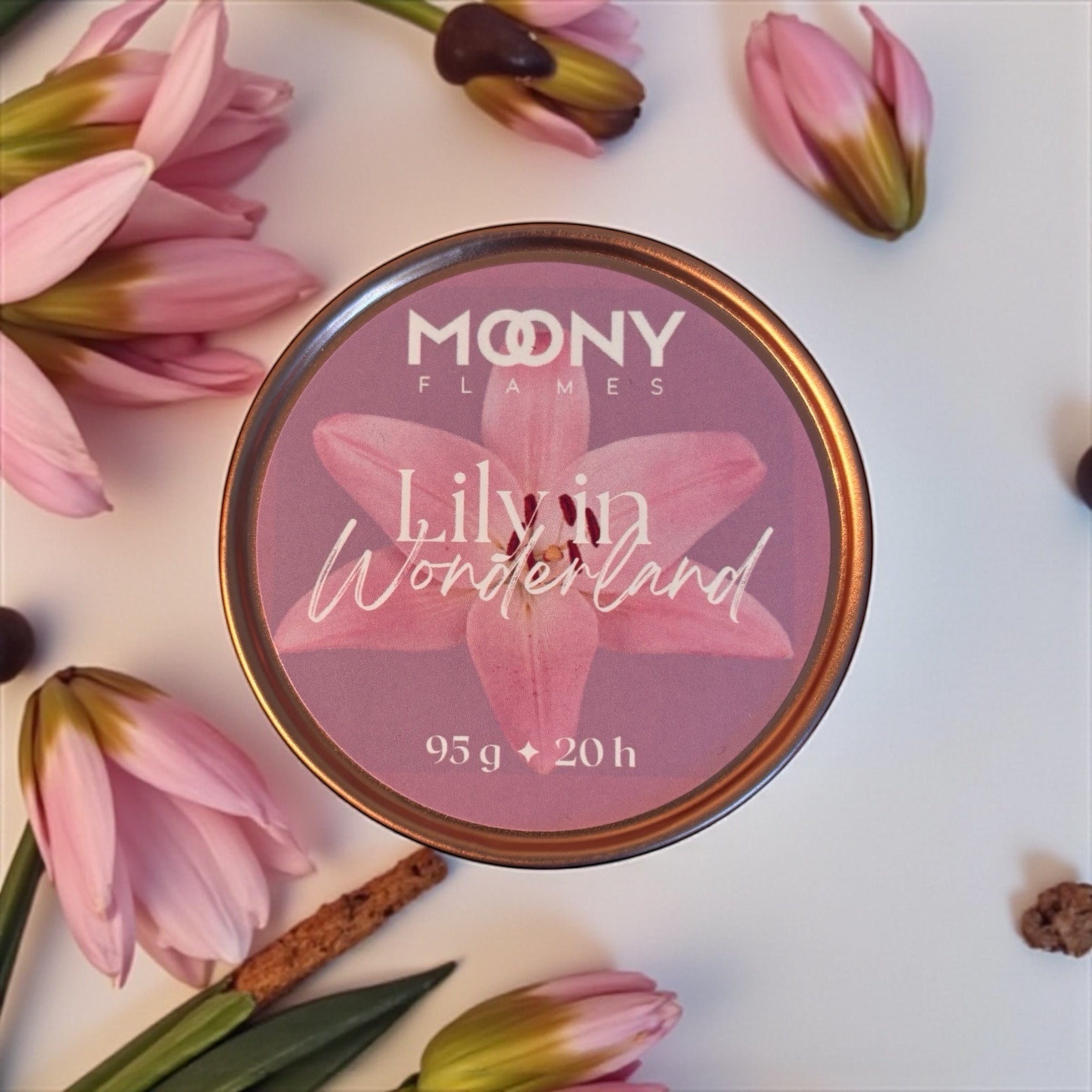 Doftljuset Liliy in Wonderland från Moony Flames som visas uppifrån på en vit bakgrund och rosa blommor runt. 