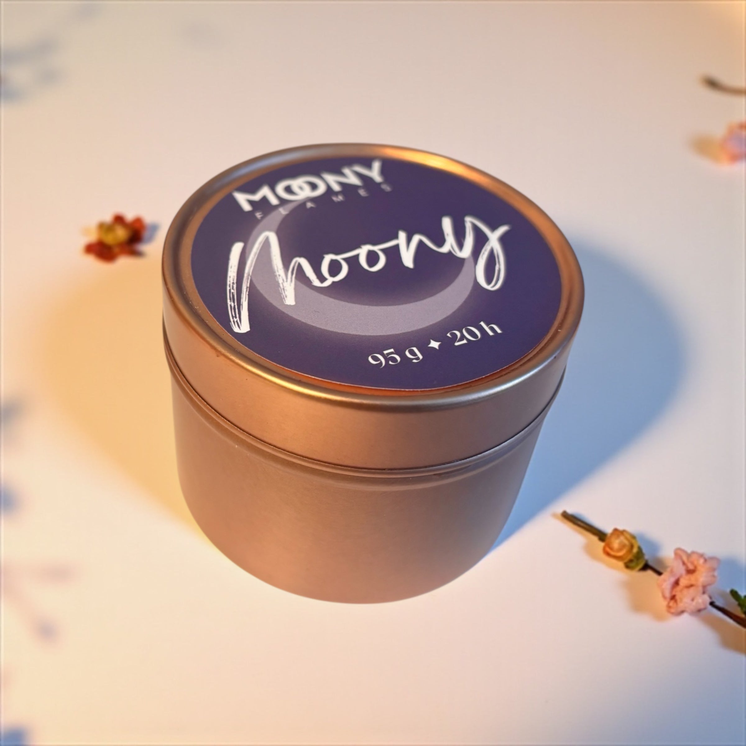 Bilden visar doftljuset Moony från Moony Flames i en metallburk i roséguld som står på en vit undergrund. och är fotograferat lite från sidan. 