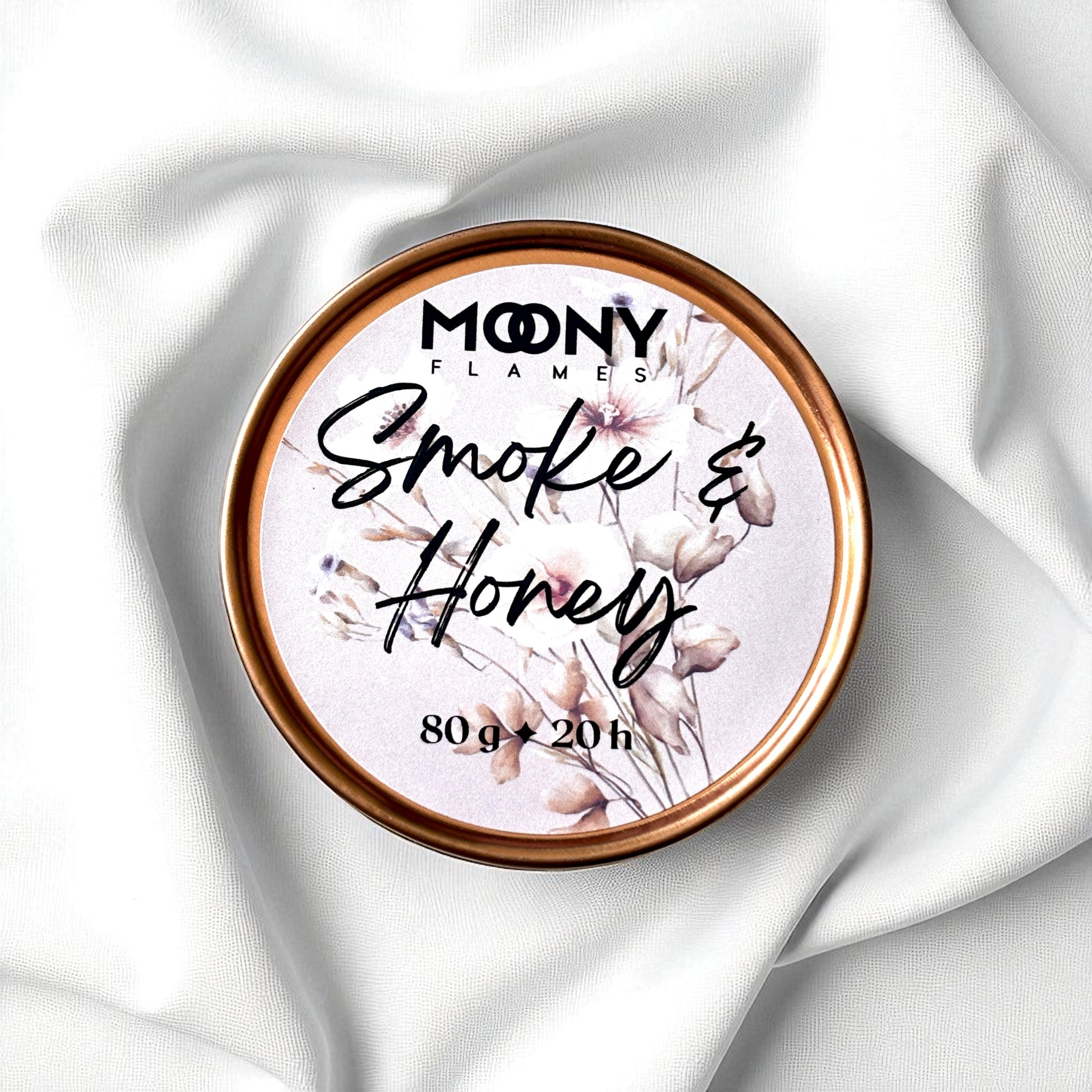 Doftljus Smoke & Honey i roséguld metallburk som ligger på en vit duk. Reseljus - Moony Flames
