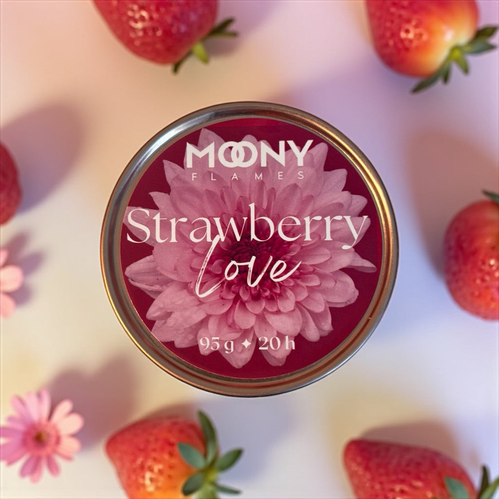 Bilden visar doftljuset Strawberry Love från Moony flames i metallburk. Ljuset syns uppifrån och står på en vit undergrund med några jordgubbar runt sig. 