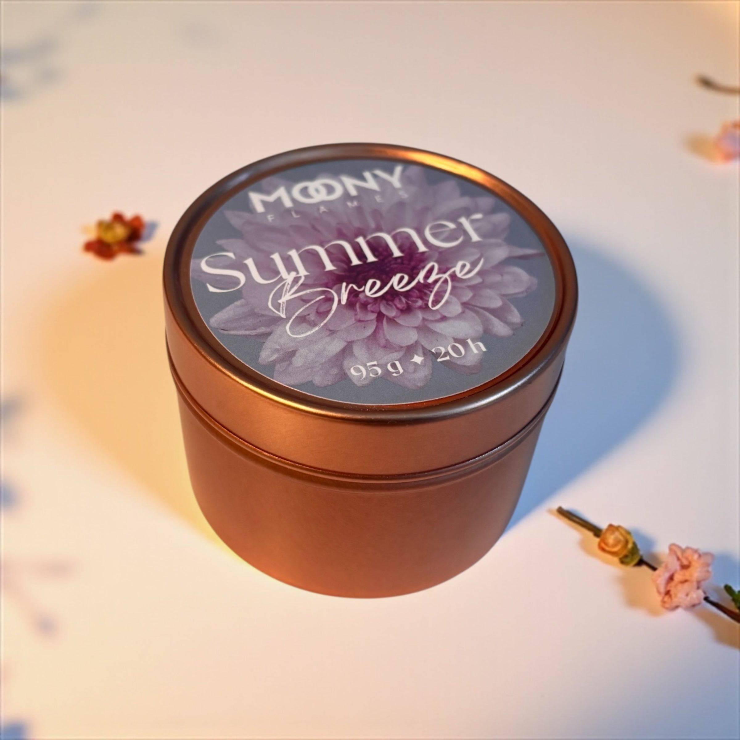 Reseljus Summer Breeze från Moony Flames visas på denna bild. Metallburken i roséguld visas lite från sidan, ståendes på en vit undergrund med små blommor runt sig. 