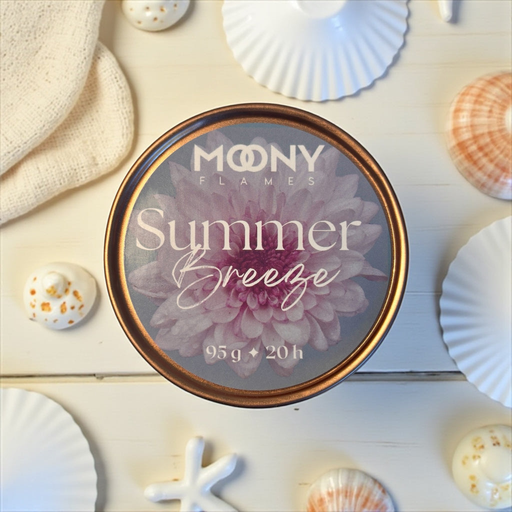 Reseljus Summer Breeze från Moony Flames visas på denna bild. Metallburken i roséguld visas uppifrån, ståendes på ett vitt träbord med några musslor runt sig. 