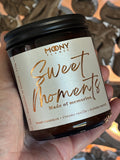 Doftljus Sweet Moments i glasburk i amber med skimrande etikett och svart lock. Ljuset hålls i handen - Moony Flames.