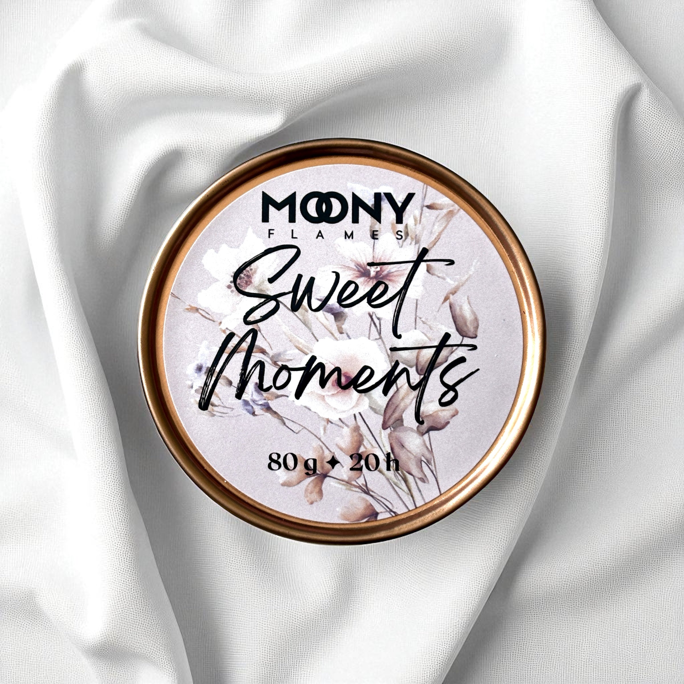 Doftljus Sweet Moments i roséguld metallburk som ligger på en vit duk. Reseljus - Moony Flames