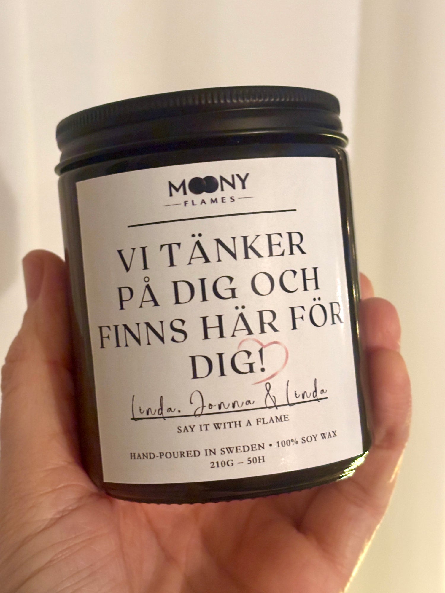 Personligt doftljus med budskap från Moony Flames som hålls i handen framför en ljus bakgrund.