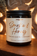 Handgjort doftljus Smoke & Honey från Moony Flames i amberglas med etikett i varma toner, placerat på träyta med mjuk och stämningsfull bakgrund.