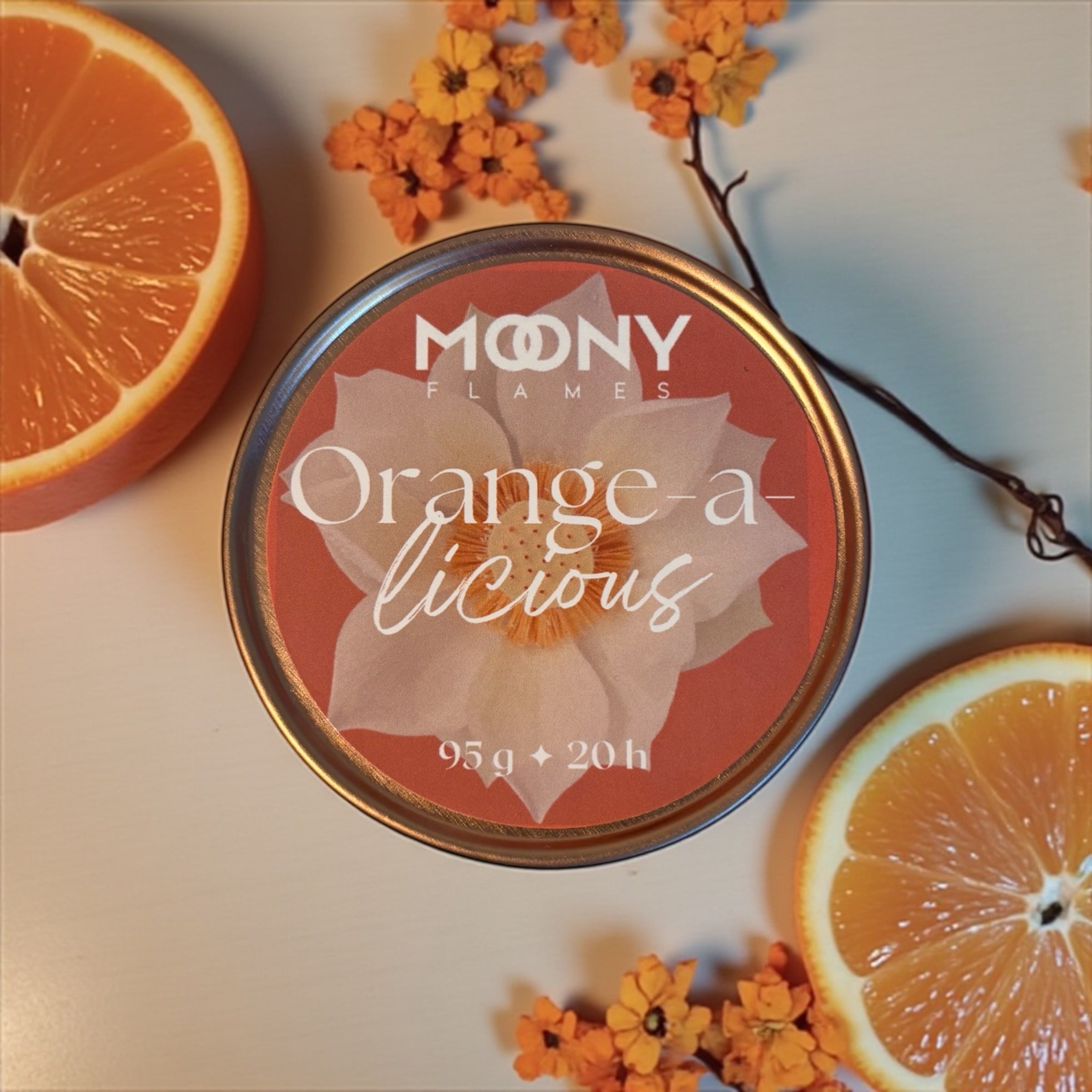 På bilden ser man doftljuset Orange-a-licious fotograferat uppifrån med några apelsinskivor och små oranga blommor runt sig.