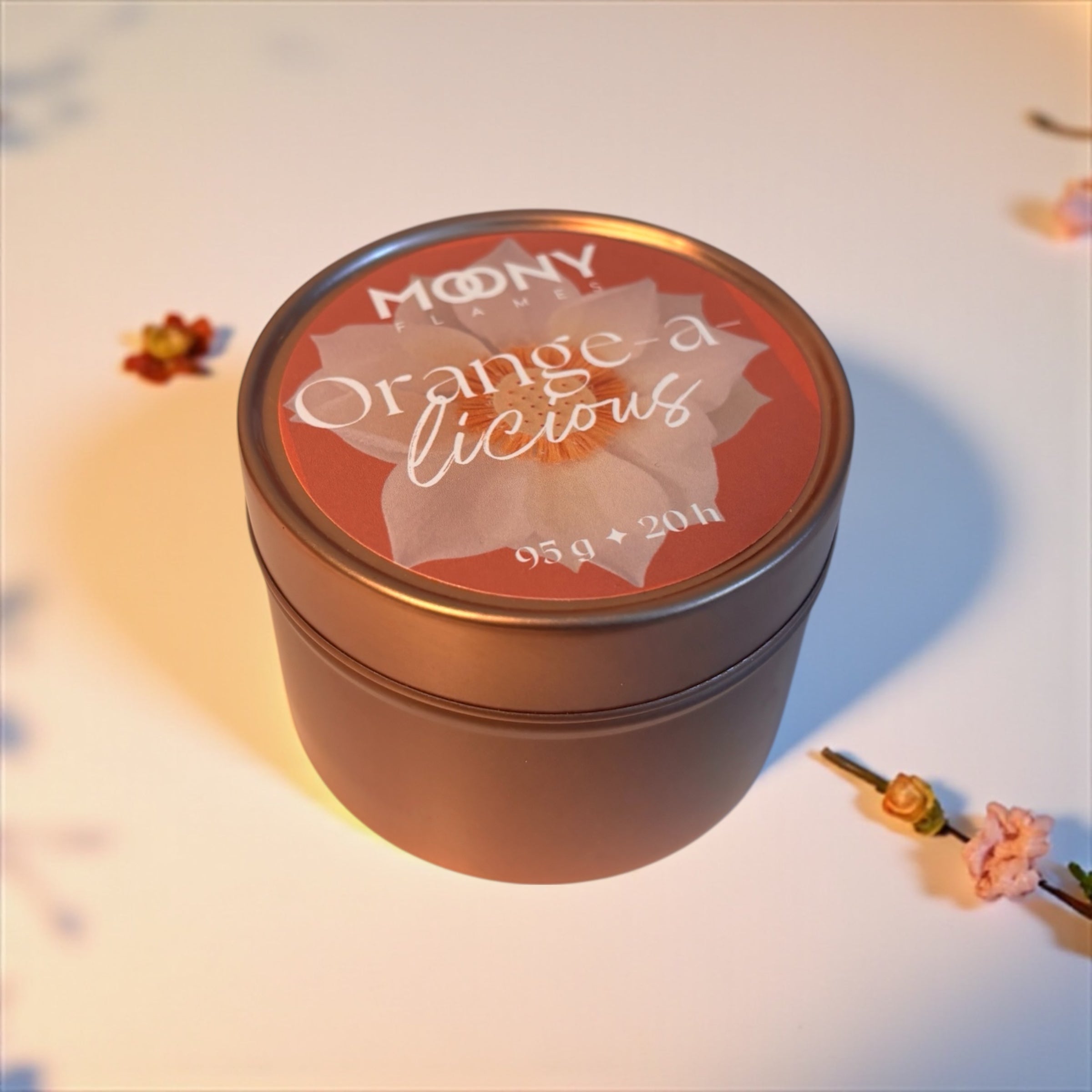 På bilden ser man doftljuset Orange-a-licious i en metallburk i roséguld lite från sidan ståendes på en vit bakgrund.