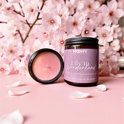 Ljuset i amber glasburk står på en rosa duk med många körsbärsblommor i bakgrunden. Det visas även en liggande burk så att själva ljuset syns bredvid. 