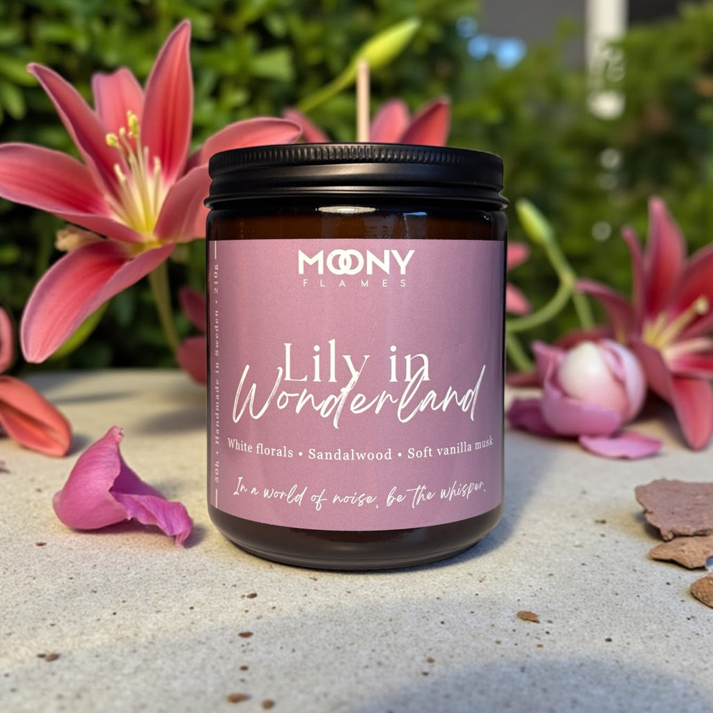 Doftljuset Lily in Wonderland från Moony Flames i amberglas, placerat i solsken på en sten med rosa liljor i bakgrunden.