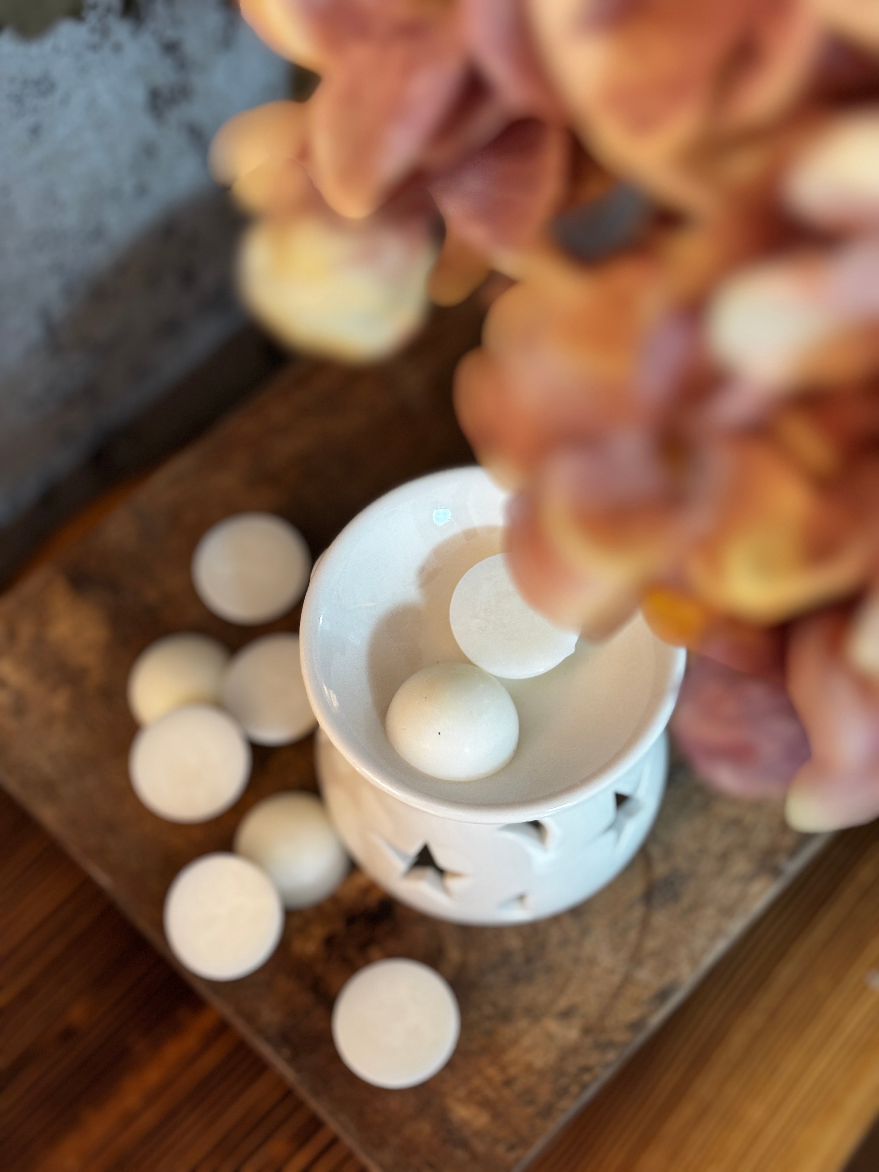 Man ser doftpralinerna ligga i en aromalampa uppifrån. Lampan står på ett rustikt träbord och det syns torkade stora blommor lite vid sidan.