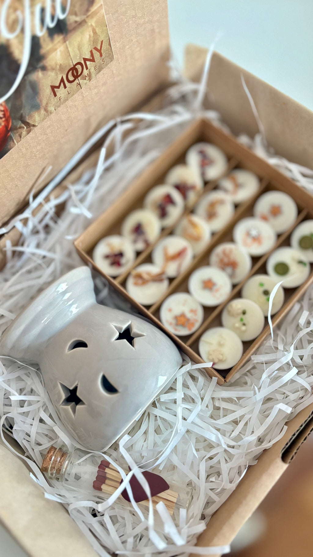 Moony Flames presentlåda som syns uppifrån. Det ligger en liten aromalampa i den samt en öppnad aks med doftpraliner som är fint dekorerade.