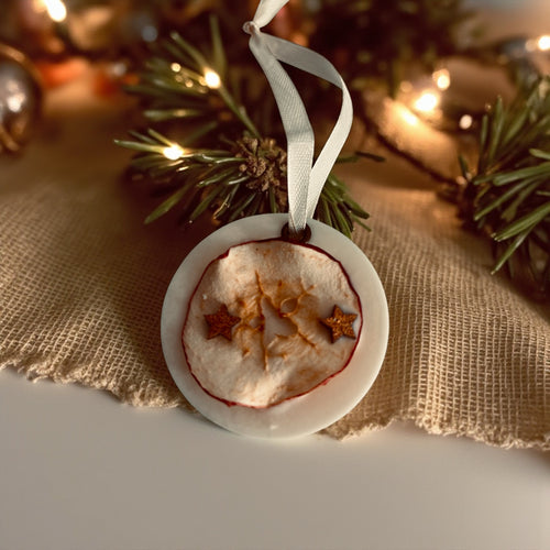 Doftvaxhängare med äppeldekoration som ligger på ett bord som är dekorerad med grankvist och ljusslinga. 