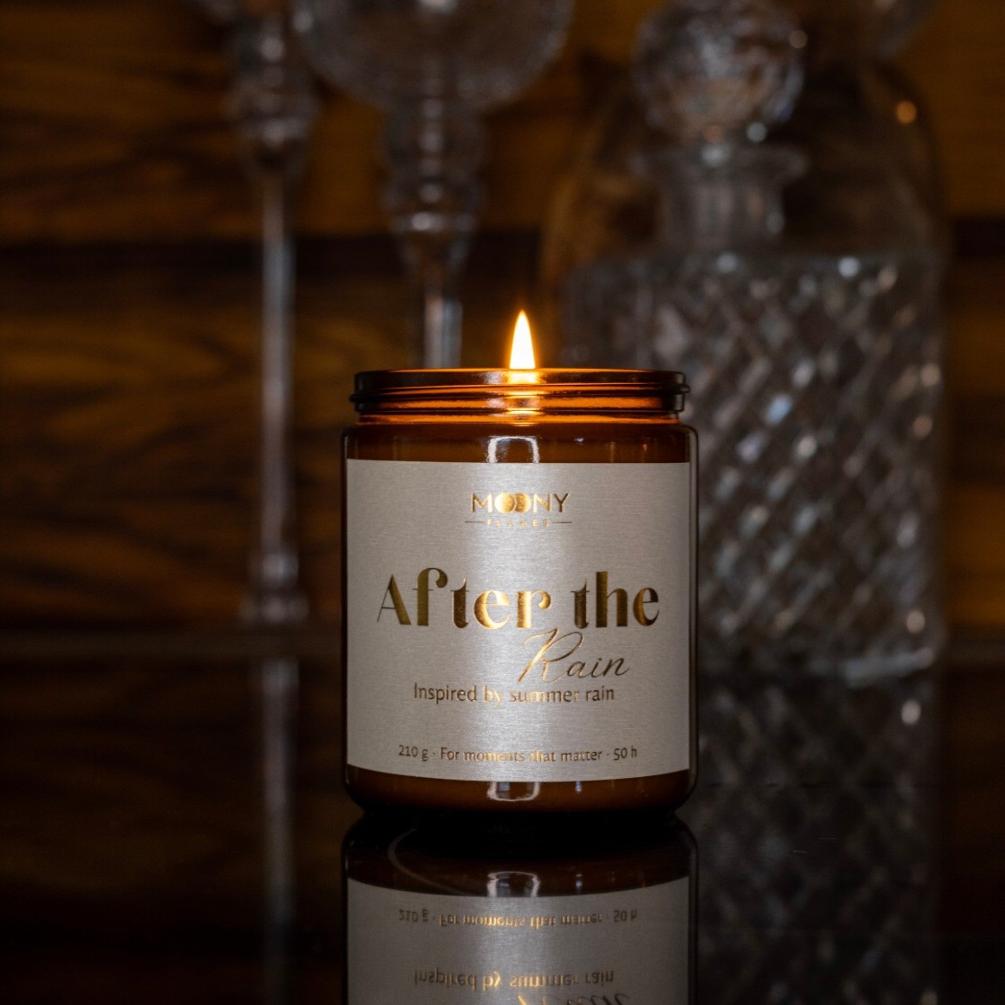 Handgjort doftljus After the Rain i brun glasburk som brinner i mörk miljö med reflektion – varm och elegant atmosfär.