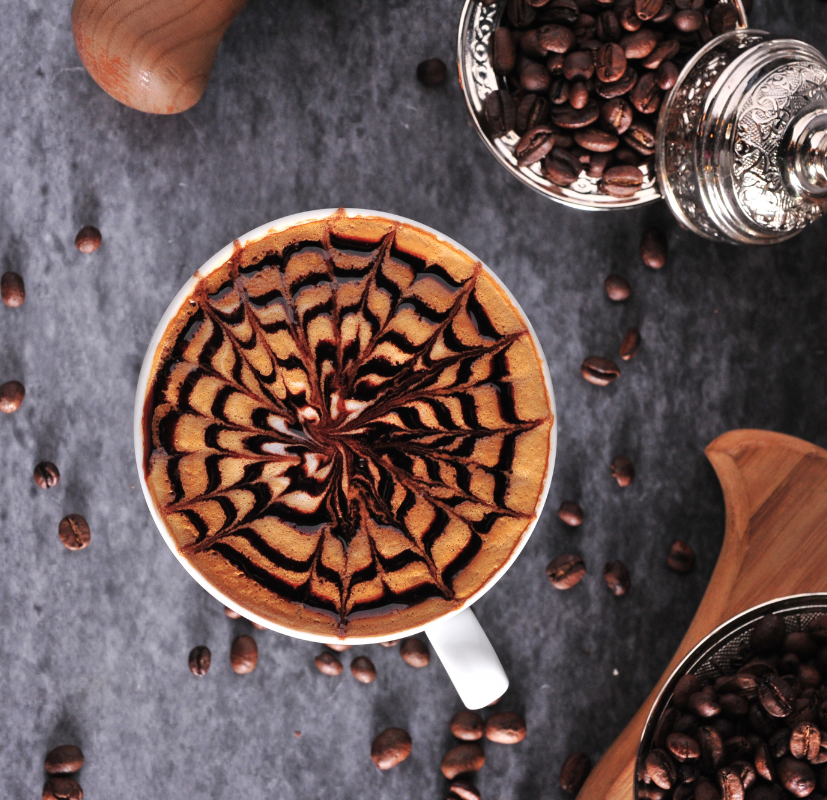 Kopp med krämigt kaffe och kaffebönor som illustrerar den varma doften i doftljuset Coffee O’Clock från Moony Flames.