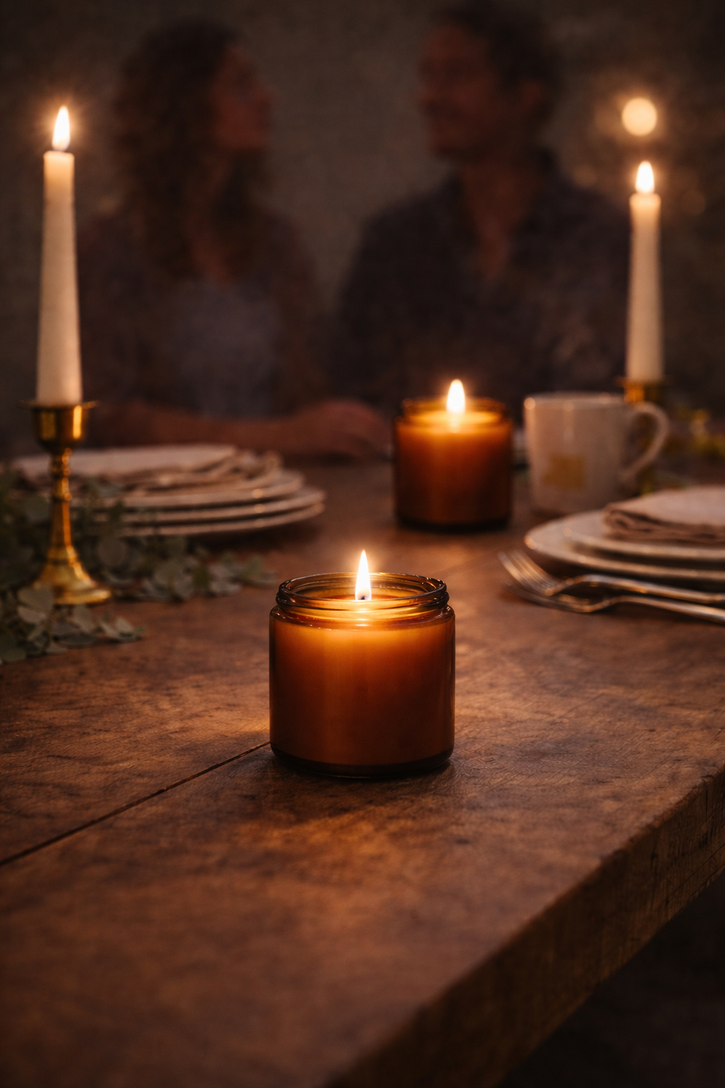 Tända handgjorda doftljus i amberglas på dukat träbord, som skapar varm och intim stämning vid en middag i mjukt ljus.