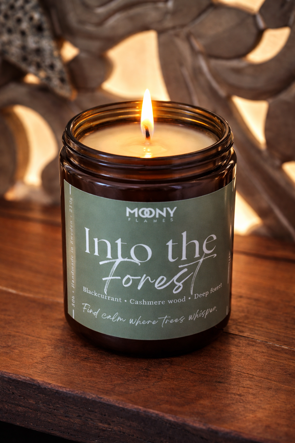 Brinnande Into the Forest doftljus från Moony Flames i amberglas, med rogivande noter av svarta vinbär, cashmere wood och djupa skogstoner.