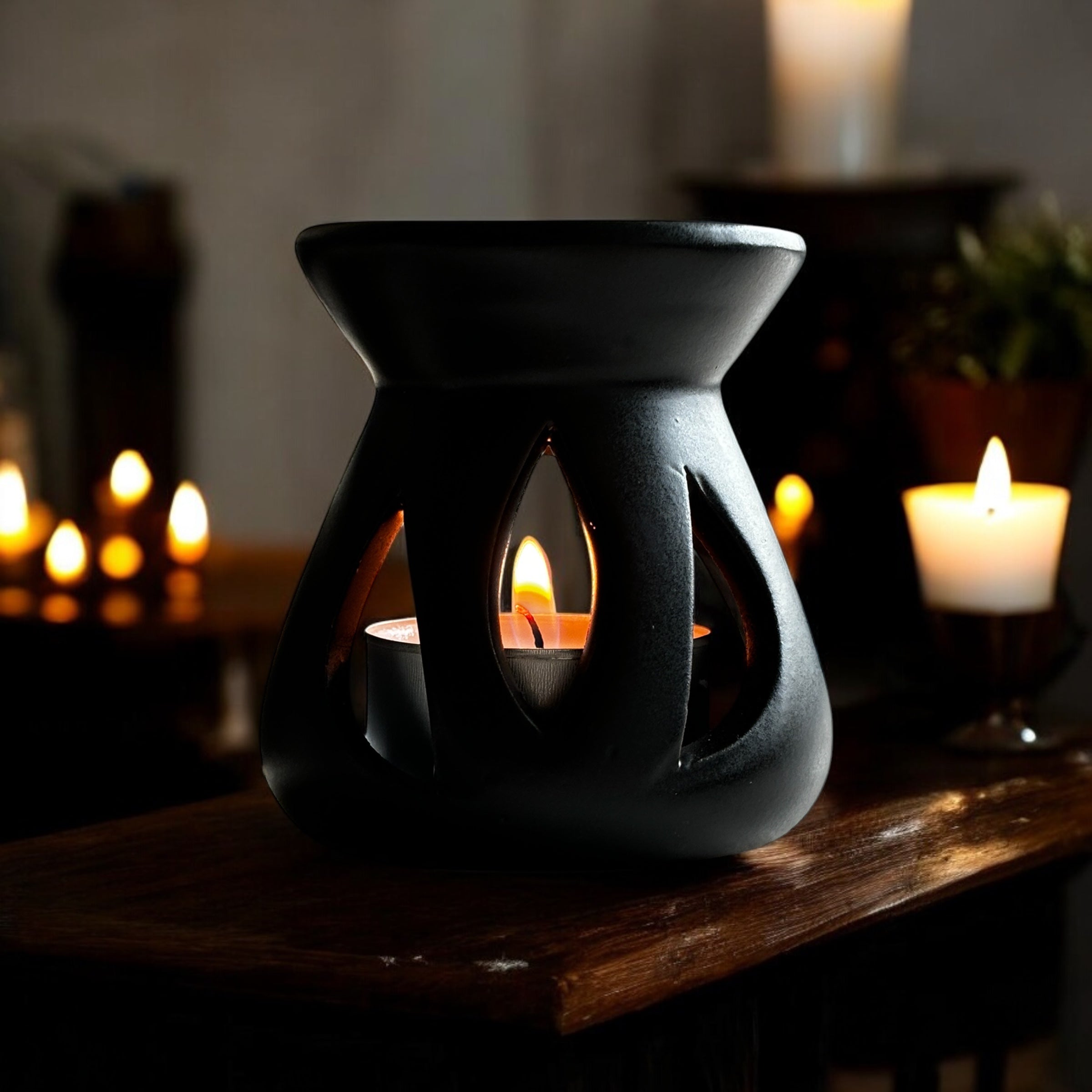 Black Lotus aromalampa i svart keramik – liten doftlampa för doftvax och eteriska oljor som sprider ett mjukt ljus och behaglig doft och som står på en rustik hylla med några tända ljus.