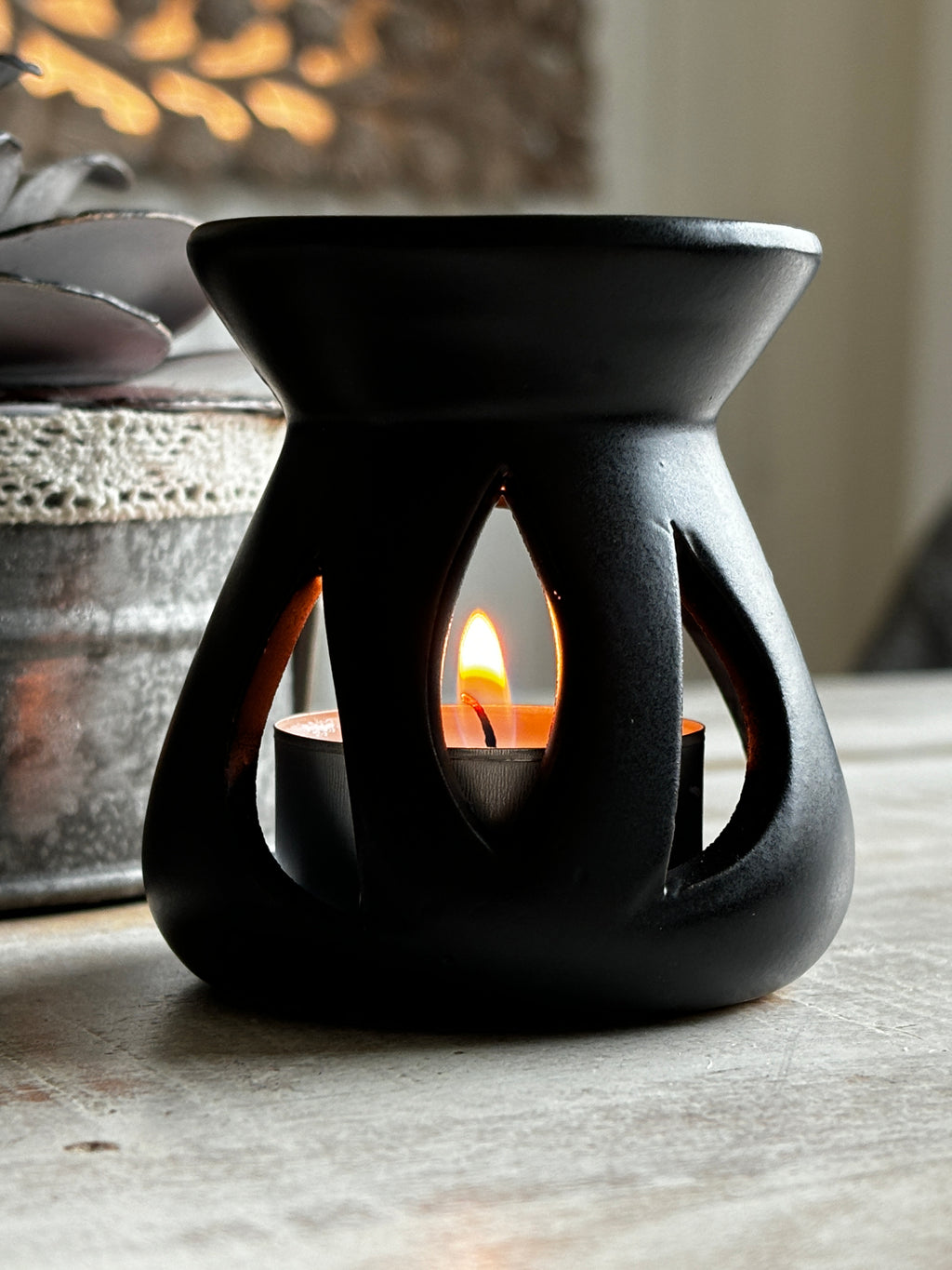 Black Lotus aromalampa i svart keramik – liten doftlampa för doftvax och eteriska oljor som sprider ett mjukt ljus och behaglig doft, står på ett träbord.