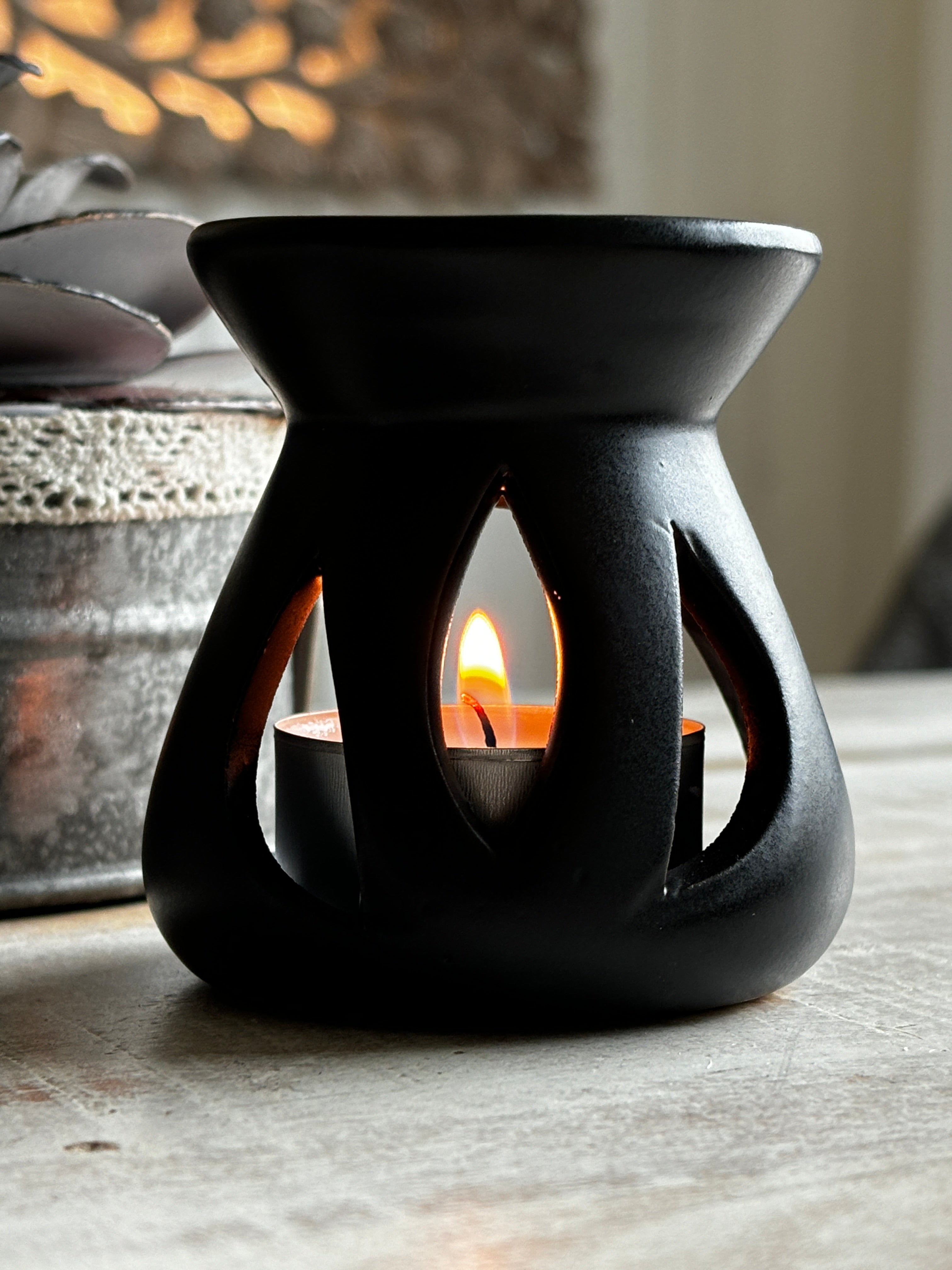Black Lotus aromalampa i svart keramik – liten doftlampa för doftvax och eteriska oljor som sprider ett mjukt ljus och behaglig doft, står på ett träbord.