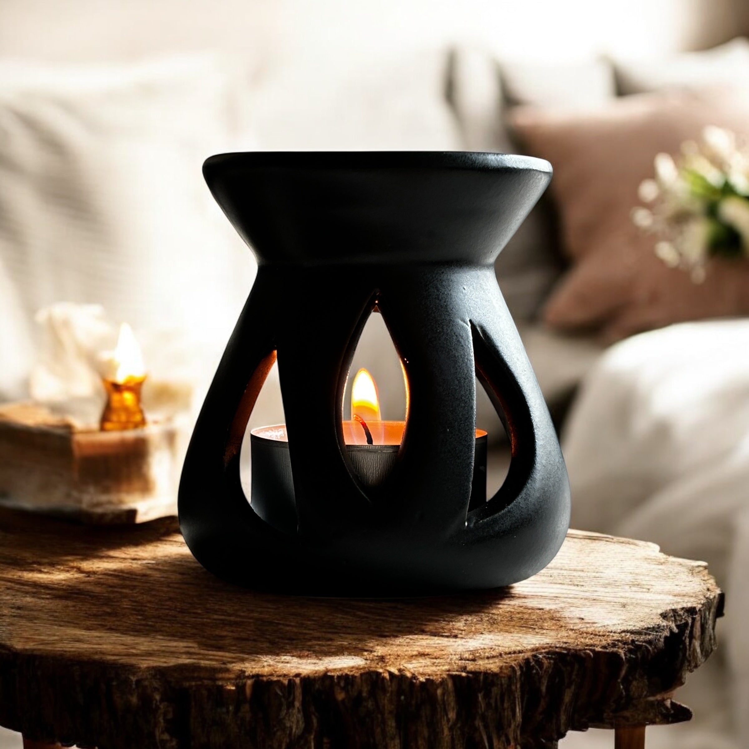 Black Lotus aromalampa i svart keramik – liten doftlampa för doftvax och eteriska oljor som sprider ett mjukt ljus och behaglig doft och står på en rustik träskiva med en soffa i bakgrunden.