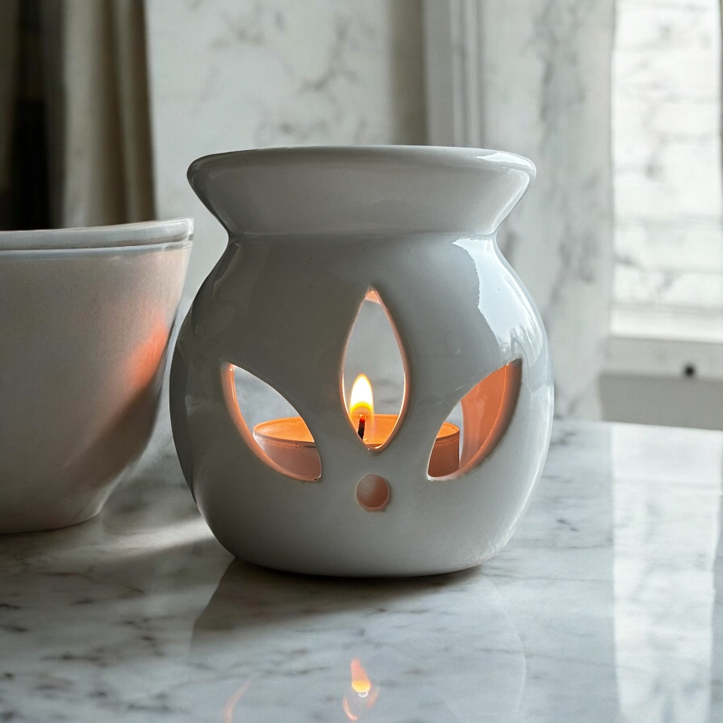 White Lotus aromalampa i vit keramik – liten och elegant doftlampa för doftvax och eteriska oljor som står i ett ljust badbrum på en marmorskiva. Det syns ett fönster i bakrunden.