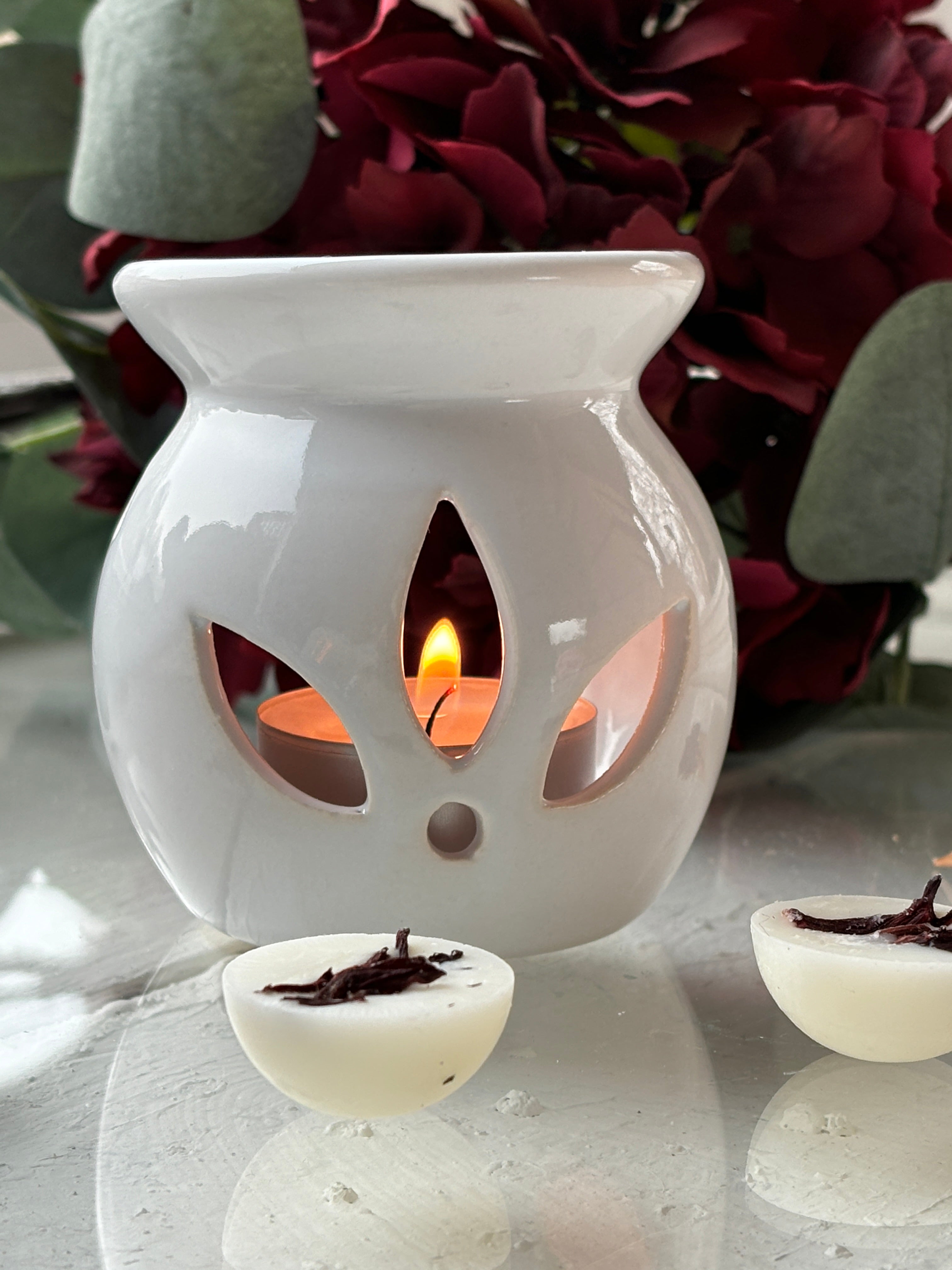 White Lotus aromalampa i vit keramik – liten och elegant doftlampa för doftvax och eteriska oljor, med blomma i bakgrunden.