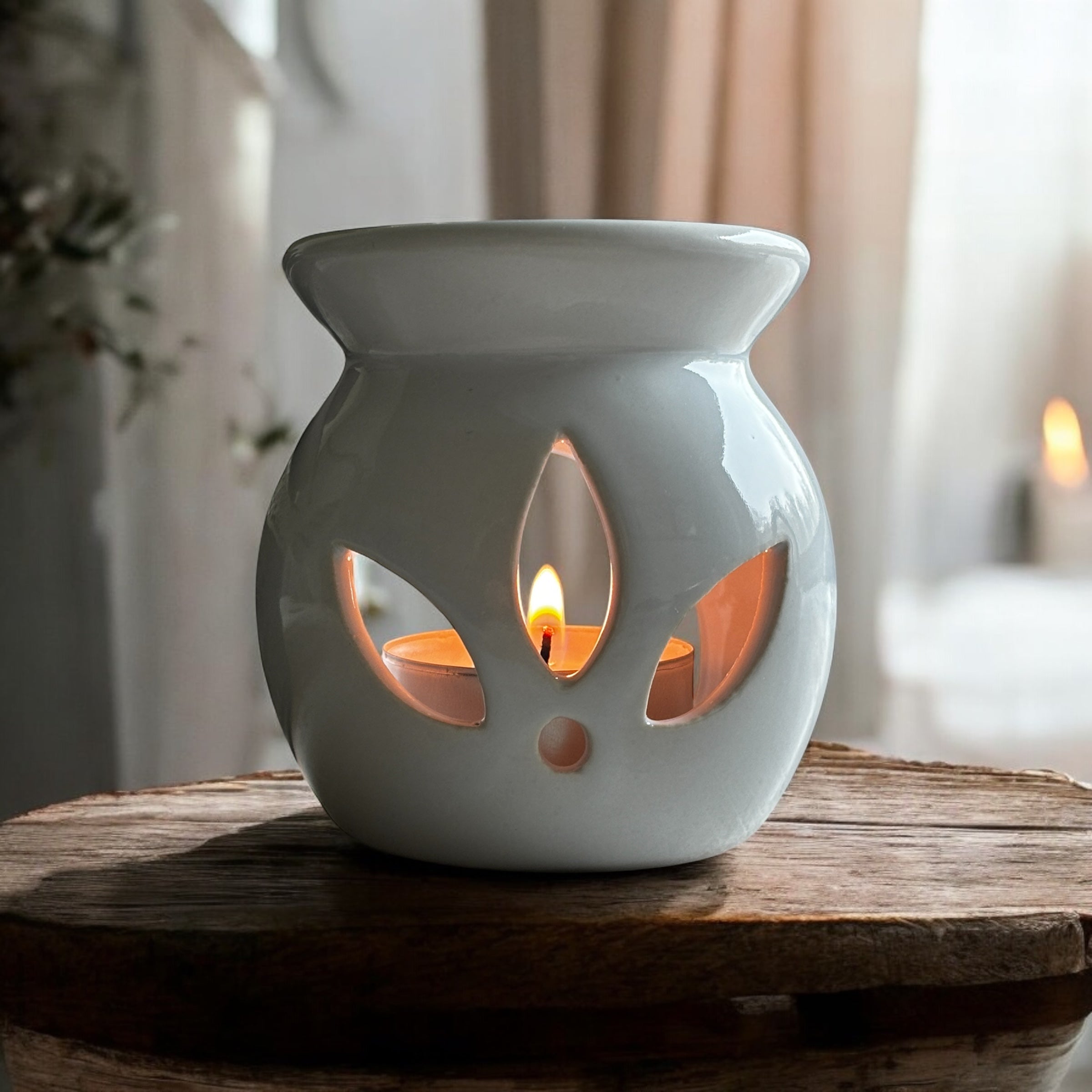 White Lotus aromalampa i vit keramik – liten och elegant doftlampa för doftvax och eteriska oljor och som står på en rustik träskiva. Ett fönster syns i bakgrunden.