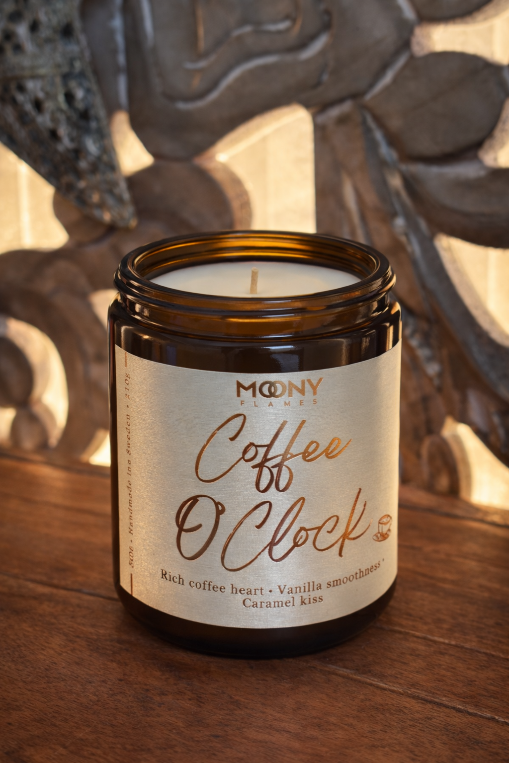 Handgjort doftljus med kaffedoft Coffee O’Clock från Moony Flames i amberglas med etikett i varma toner och mjuk, stämningsfull bakgrund.