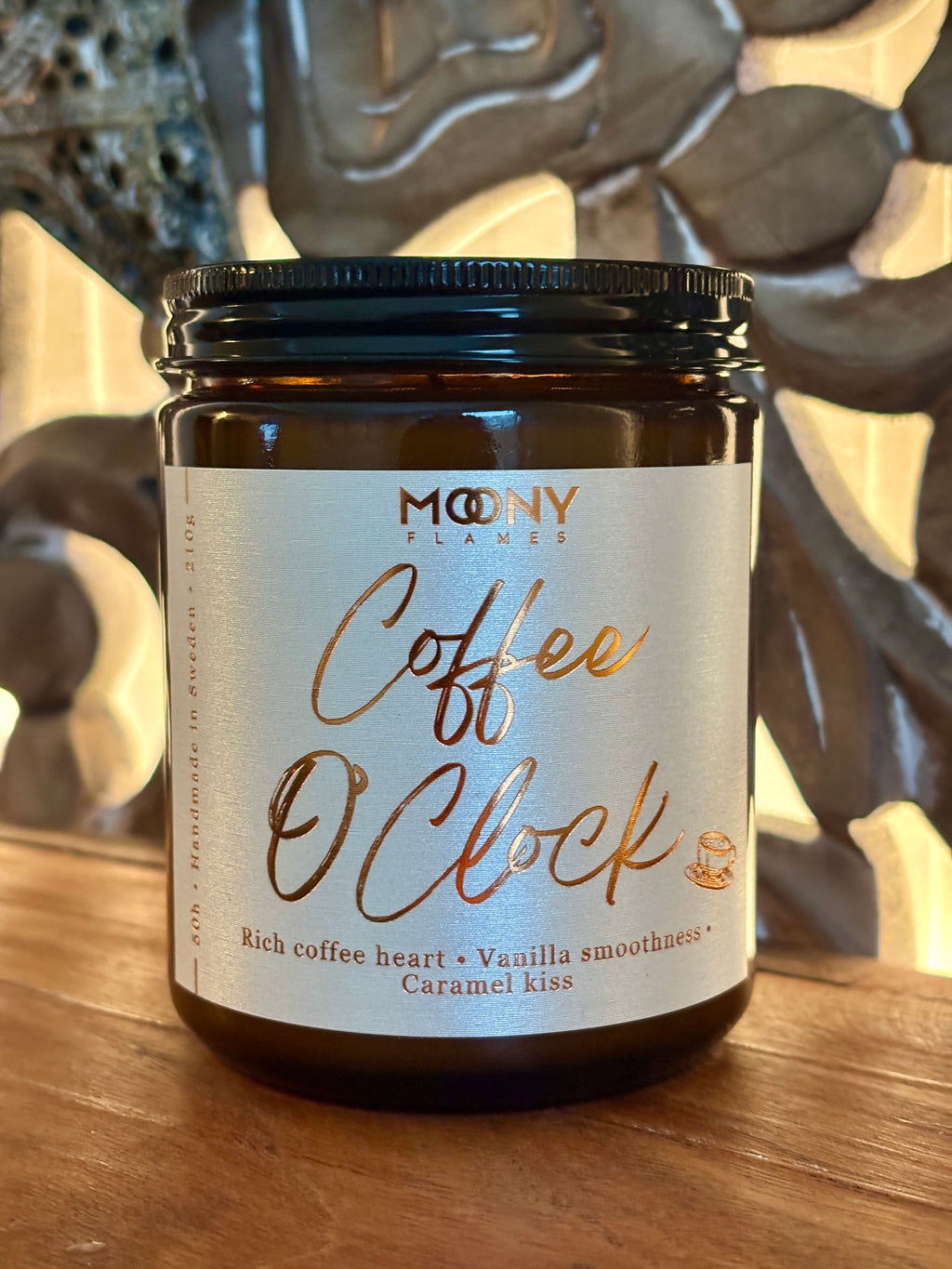 Handgjort doftljus Coffee O’Clock från Moony Flames i amberglas med etikett i varma toner, placerat på träyta med mjuk, stämningsfull bakgrund.