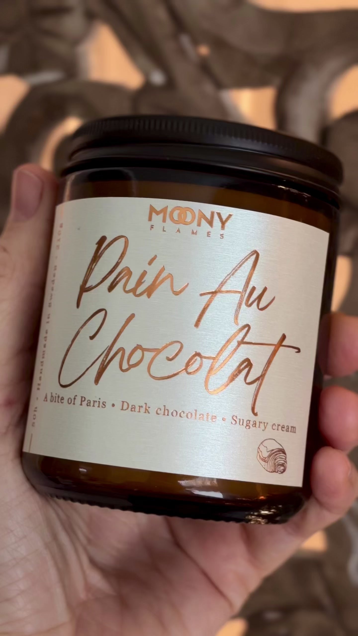 Pain Au Chocolat doftljus från Moony Flames hålls i handen i en video  – ett varmt och krämigt gourmand-doftljus med noter av mörk choklad och söt grädde, inspirerat av Paris.