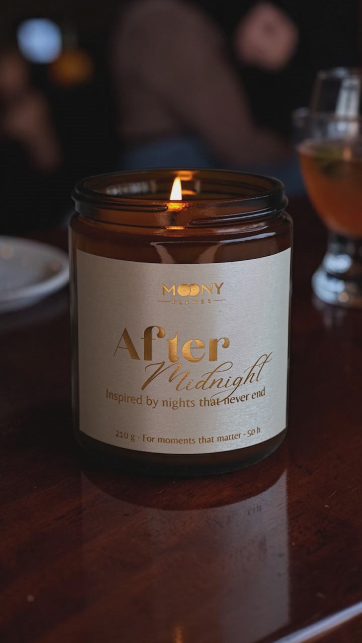 Handgjort doftljus After Midnight i brun glasburk som brinner på ett bord i kvällsmiljö, med suddiga ljus och drink i bakgrunden – varm, sensuell atmosfär.