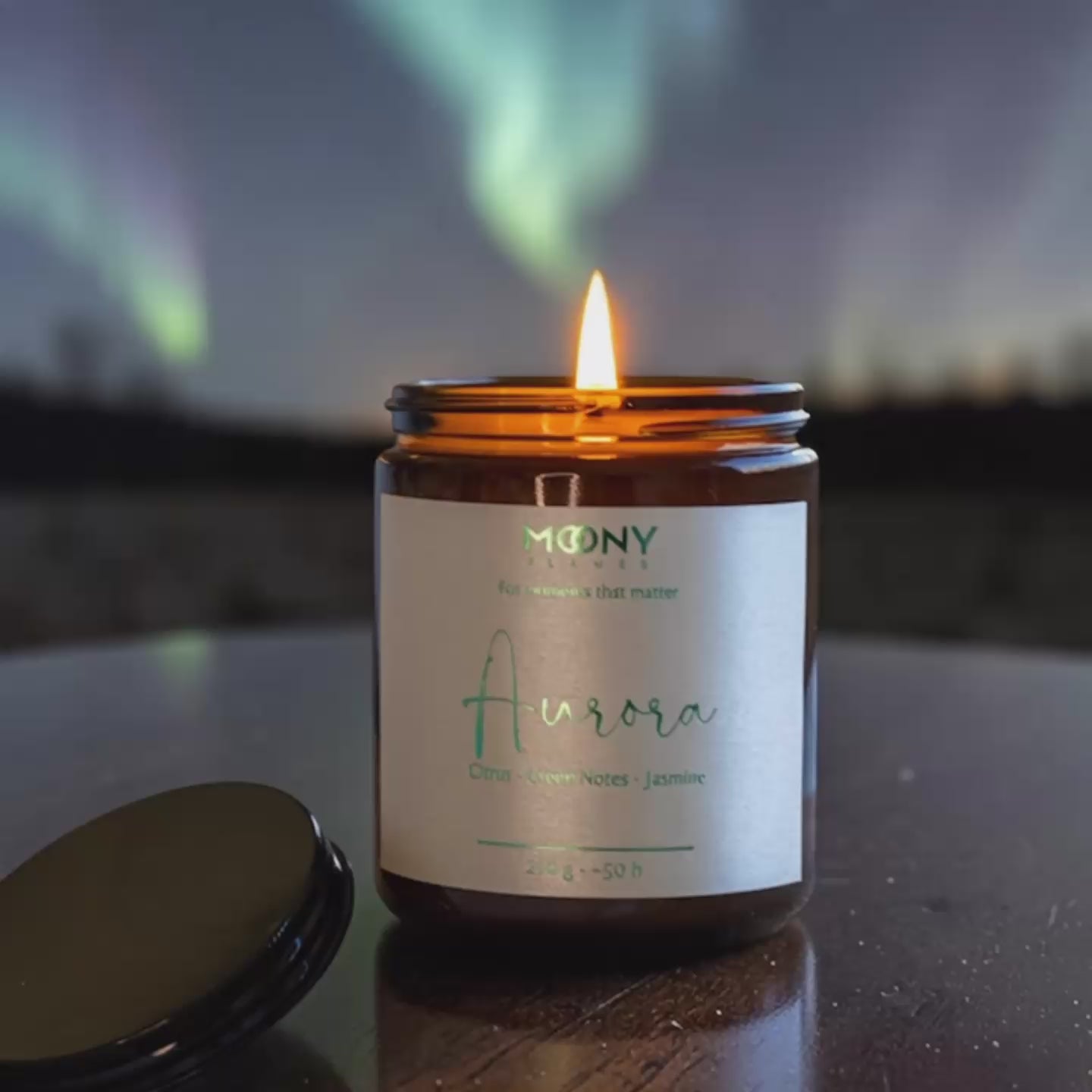 Handgjort doftljus i glasburk med svart lock, tänt framför fönster med norrsken utanför – stämningsfullt ljus inspirerat av lugna ögonblick