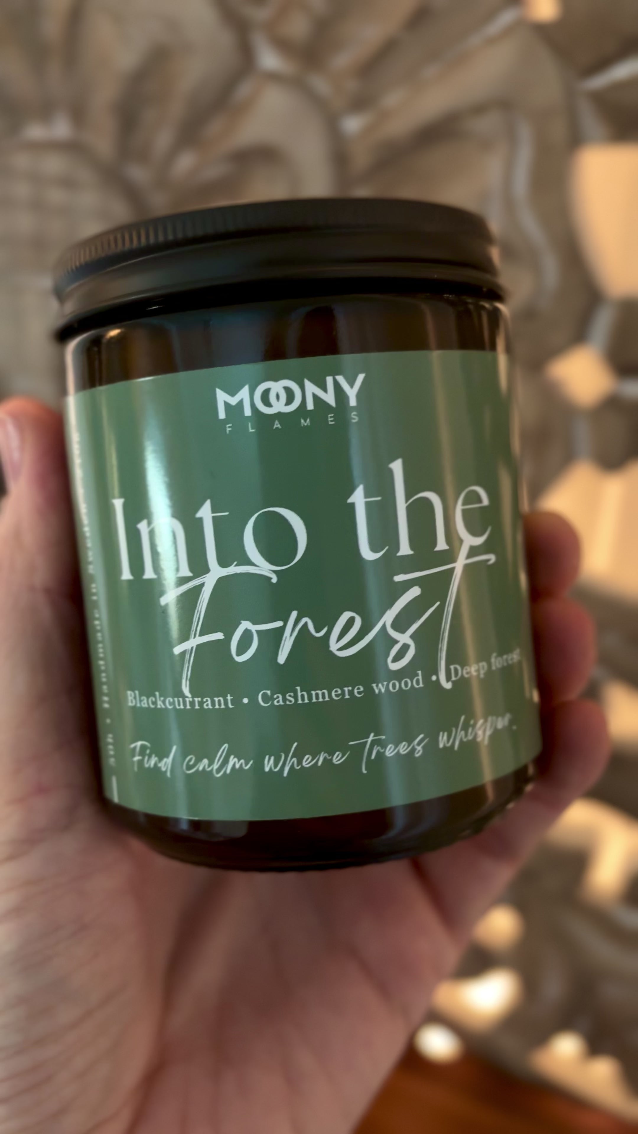 Into the Forest doftljus från Moony Flames hålls i handen – ett rogivande, grönt doftljus med noter av svarta vinbär, cashmere wood och djupa skogstoner.