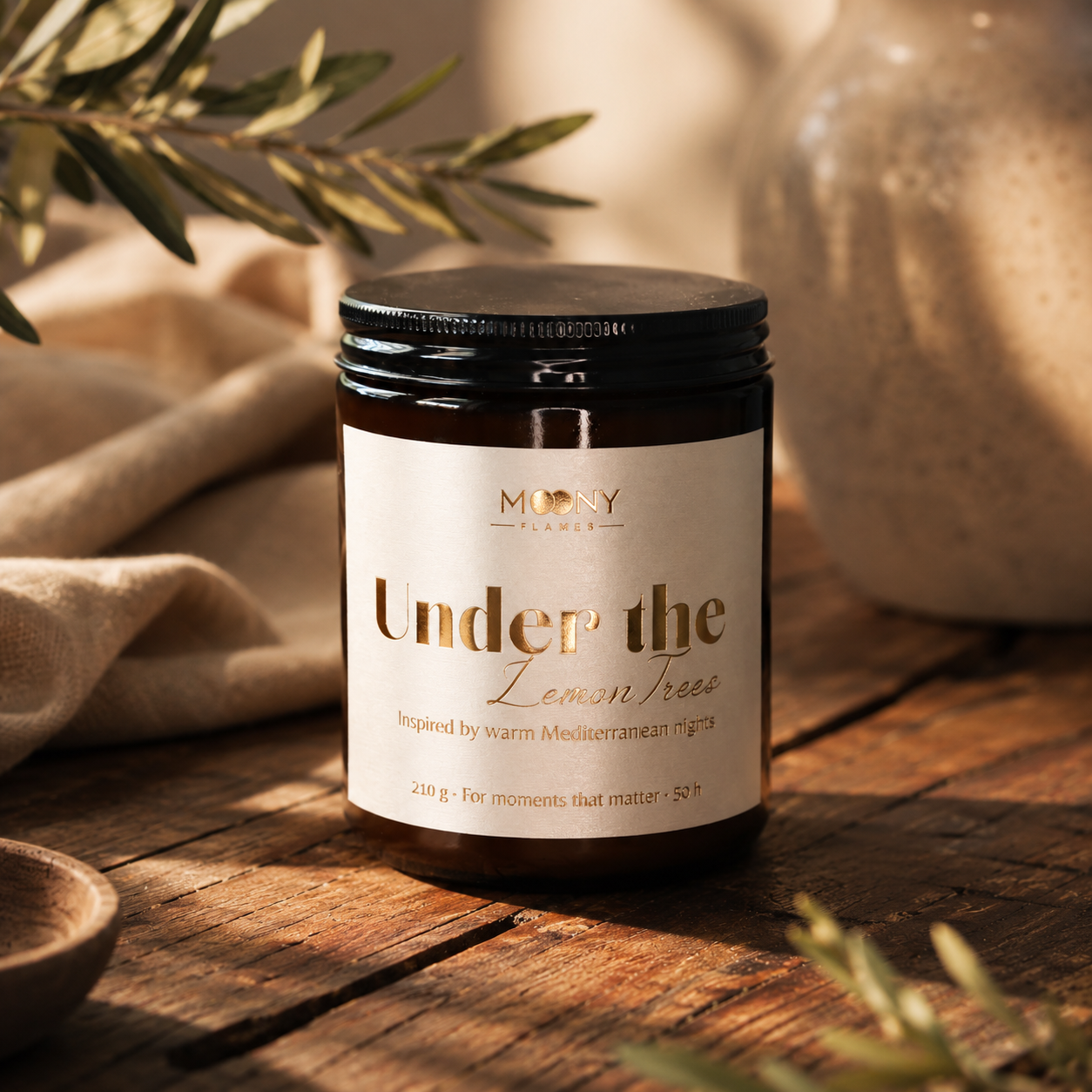 Under the Lemon Trees doftljus från Moony Flames på rustikt träbord med olivkvistar och varm medelhavsinspirerad inredning. Handgjort doftljus med frisk citrus, gröna noter och aromatiska örter, tillverkat i Småland, Sverige.