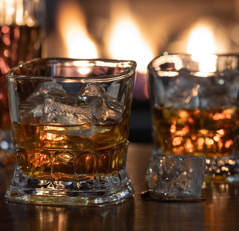 Whiskeyglas framför en varm brasa som illustrerar den rökiga och träiga doften i doftljuset Whiskey & Fire från Moony Flames.
